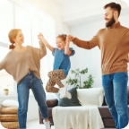 Couple holds their child’s hands and swings her above the ground between them.